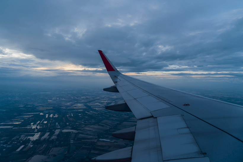 Airplane wing view at sunset over a cloudy sky, aerial landscape.