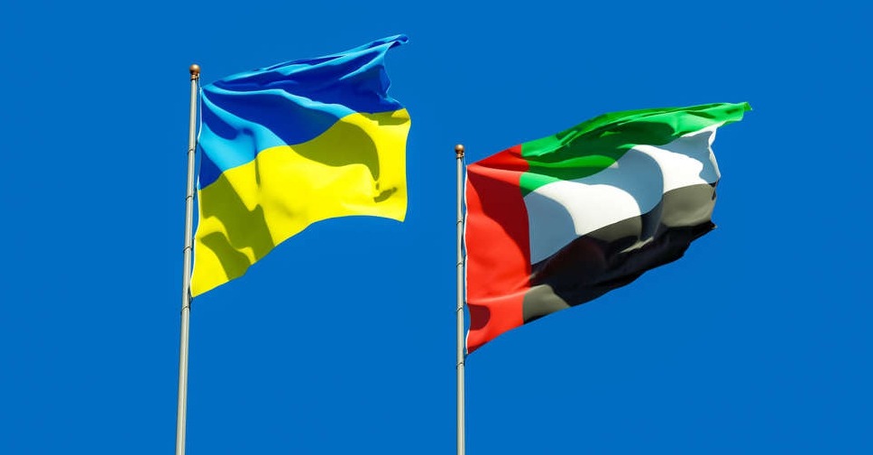 Ukrainian and United Arab Emirates flags waving together against a clear blue sky, symbolizing international relations and cooperation.